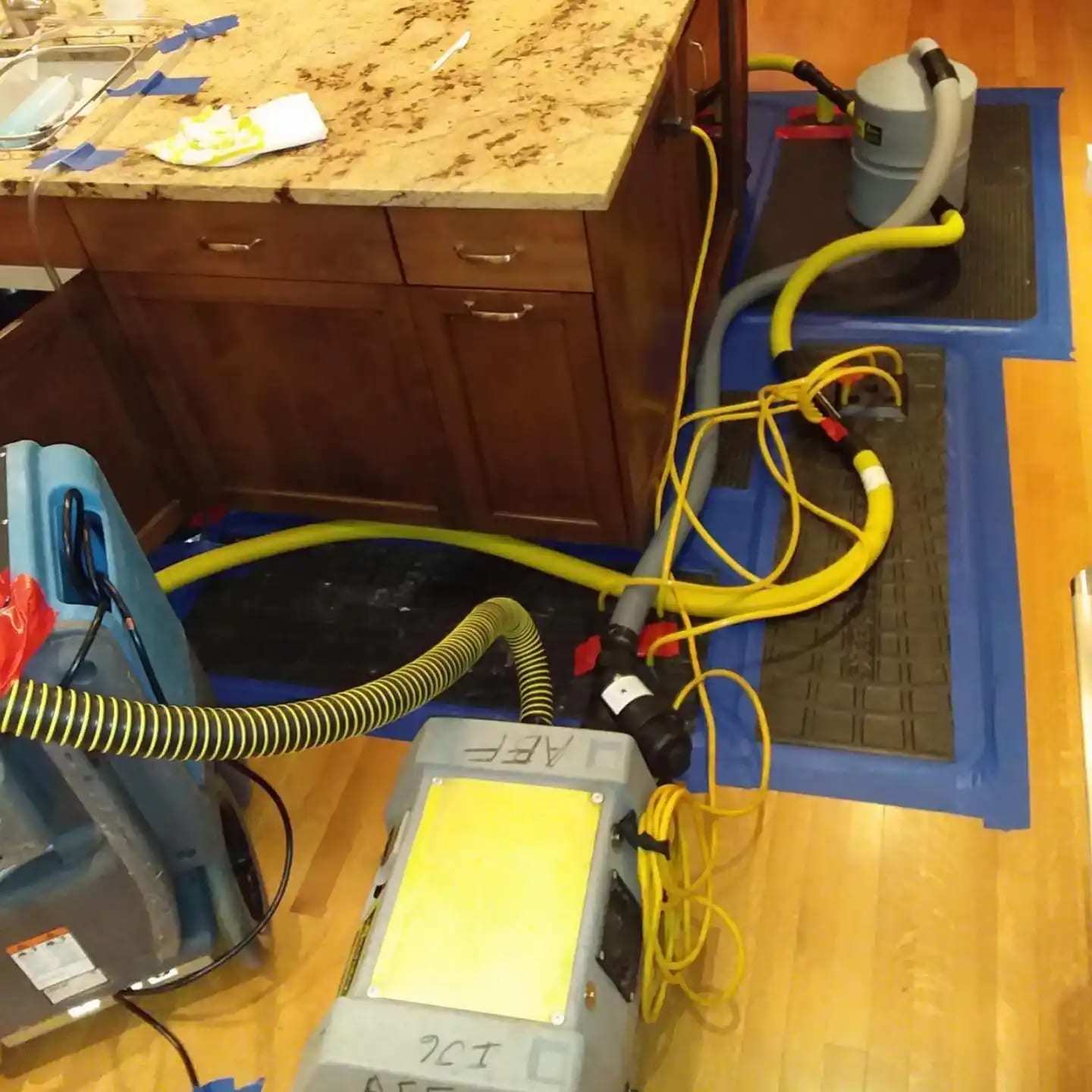 Floor drying mats and hoses on a kitchen floor beside the cabinets