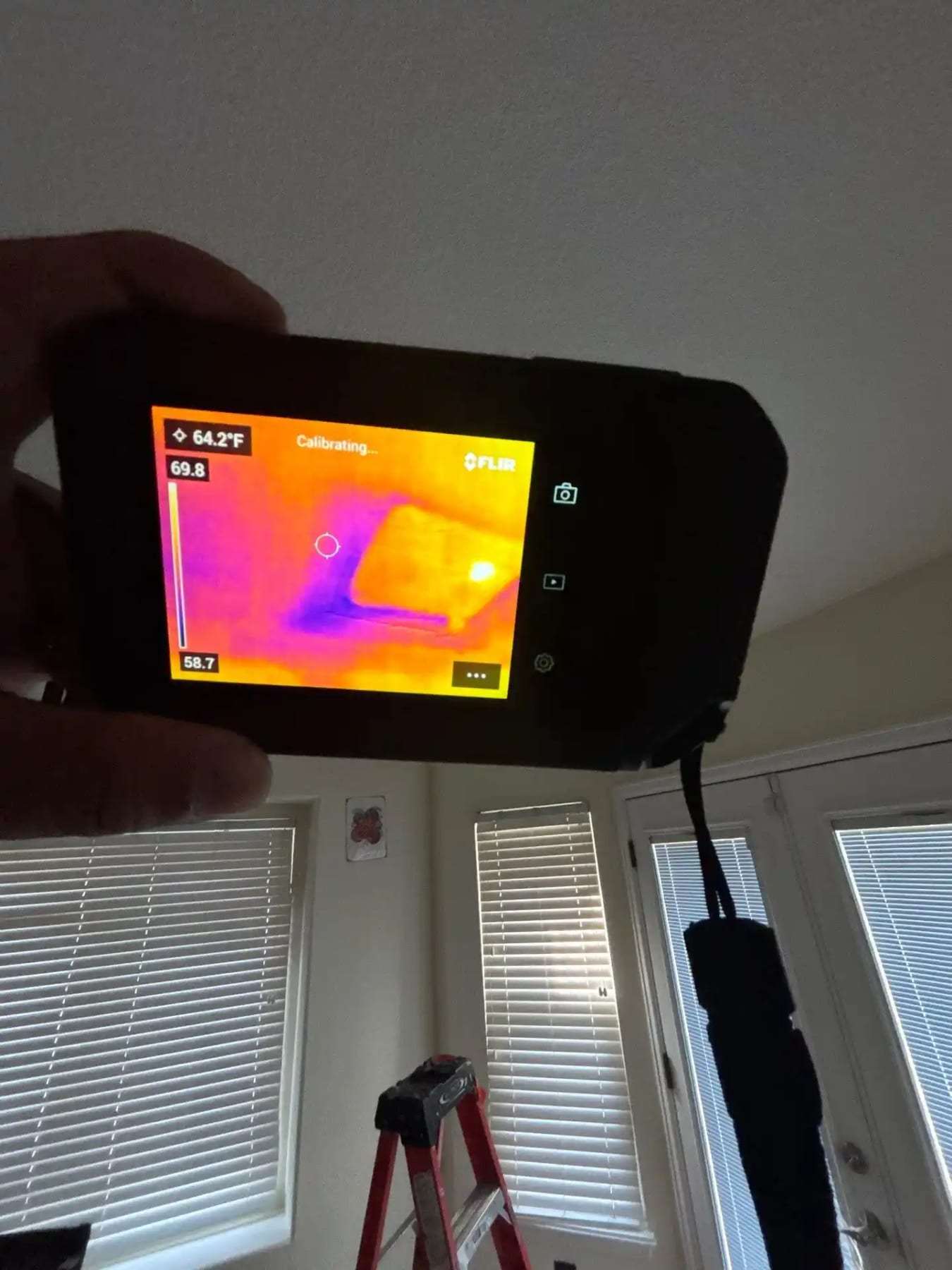 Thermal imaging camera held up in a sunroom with blinds